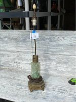 Full view of the antique Asian jade and brass lamp standing upright on a textured white surface.