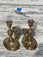 Pair of antique silver-plated candlesticks on wooden surface with visible tarnishing and detailed designs.
