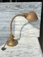 Full view of the antique brass desk lamp showing base, gooseneck arm, shade, and attached cord on a light wooden surface.