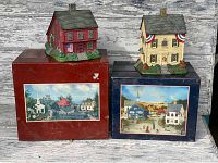 Both folk art village houses displayed on their original boxes with countryside scene labels on fronts.