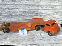 Full side view of orange cast metal truck cab connected to flatbed trailer