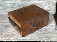 Photo showing the top and two sides of the heavy rectangular wooden butcher block with a brass handle and black metal reinforcement.