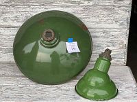 The pair of vintage industrial porcelain light shades. Larger shade is flat on one side, smaller shade has a rounded top and visible metal fixture.