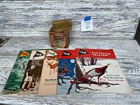 Photo showing six vintage 'TAM Archery World' bow hunting magazines lined up with two antique shot shell boxes behind.