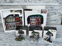 Full lot display of the Department 56 Harley-Davidson building and four boxed miniature motorcycle figures, all arranged on a rustic wooden surface.
