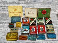 Large lot of antique tobacco tins arranged on a wooden surface showing brand names and designs.