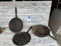 Lot of four antique cast iron skillets arranged on weathered wooden surface, showing ribbed grilling pans and traditional skillets with handles