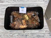 Black plastic tub filled with assorted antique metal hinges of various types and sizes, including brass and iron finishes, and one black handle.