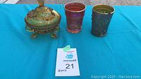 Photo showing amber pressed glass footed candy dish with lid and two Carnival Glass tumblers on a blue cloth background.
