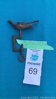 Side view of antique sewing bird clamp showing bird shape and decorative engravings.