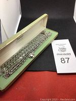 Two sterling silver charm bracelets inside a light green jewelry box, showing tea cup charm on one bracelet.