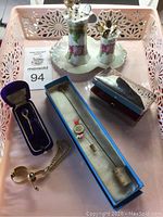 Photo showing 14 hat pins, a silver-tone floral hat pin holder with two compartments, two boxes containing additional pins including one with a blue stone pin in a velvet-lined box, and a metal chain accessory for hat pins.