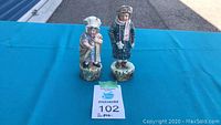 Wide front view showing two antique ceramic figurines on blue table.
