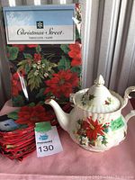 Photo showing Royal Albert Christmas teapot placed in front of packaged Christmas Street branded tablecloth and stack of red poinsettia patterned napkins.