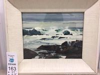 Front view of watercolor painting in white textured frame showing seascape with rocks and waves