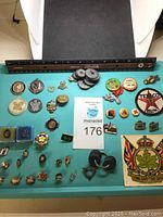 Photo showing a variety of pins, badges, and patches arranged on a blue surface with a ruler for scale. Items include award pins, Canadian maple leaf pins, and corporate logos such as Texaco.
