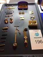 Tray with multiple men's jewelry items including tie bars, lapel pins, cufflinks, shirt studs, pocket watch chains, and purple velvet cufflink case