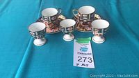 Seven piece Royal Crown Derby Imari cup set with 2 demitasse cups with saucers and 3 egg cups arranged on a turquoise cloth.