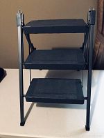 Front view of three step stepstool with black plastic solid deck steps and black metal frame.