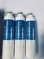 Three white EcoAqua replacement refrigerator water filters with blue label, standing upright, side by side.