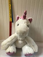 Front view of white unicorn plush toy showing purple horn and feet, sitting upright.