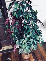 Faux tree in woven basket showing multiple colors of leaves and the tree trunk detail.