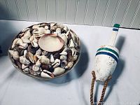 Tray filled with mixed seashells and a wooden buoy decoration on a white surface.