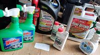 Photo of garden and cleaning supplies: 2 green bottles of Windex Outdoor, Spectracide weed killer, Ortho Home Defense insecticide Max, Roundup concentrate refill bottles, all mostly full.
