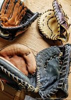 Four left-handed baseball gloves in various colors and brands arranged on wood surface.