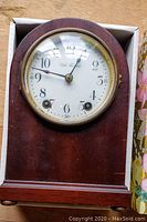 Antique Seth Thomas wooden mantel clock in box showing clock face with white dial, black numerals and hands, Seth Thomas logo, glass door and winding holes.