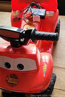 Close-up of the front of the red Lightning McQueen themed PowerWheels car showing decals, the handlebar steering, and charger on seat.