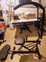 Side view of the Body-by-Jake Ab Scissor exercise machine showing seat, frame, and foot pedals in a basement storage area.