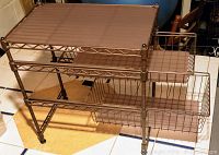 Wire two-drawer storage unit with metal wireframe and two sliding wire basket drawers, placed on tiled floor.