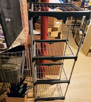 Three-tier metal wire rack with black frame, positioned in storage area, showing overall structure and included extra parts beside it.