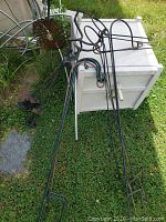 Photo showing four long metal shepherd's hooks with curved tops lying on grass beside a white cabinet and other outdoor items.