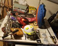 Overall lot including Razor scooters, helmets, gloves, catcher's mitts, dog tunnel, and other gear all laid out on a table.