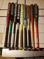 All nine Easton baseball bats arranged side-by-side on a white tile surface showing different colors and logos.
