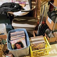 Two plastic containers filled with assorted LP vinyl records placed on floor among other household items