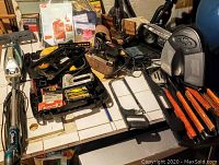 Photo showing various tools, including a Shark steamer, stapler with boxes of staples, grilling set with wooden-handled tools, belt sander with several belts, heater, TV wall mount, and radio/cassette player.