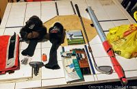 Photo of Medicus golf swing trainer iron, golf gloves (Tonic and Wilson brands), headcovers (Guinness and plain black), towel, shag-stick with balls, spike remover tool on tile table
