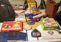 Overview of the lot showing backpack, briefcase, Mahjong set box, folded US flag, Phillies baseballs, Whitman books, and decorative dish