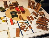 Wooden doll house furniture pieces including chairs, beds, cabinets, many parts spread out on table showing condition and variety