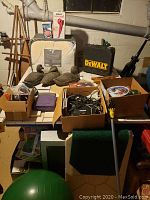 Wide view of lot items on table including duck decoys, Dewalt tool box, and assorted boxes containing electronic cables and other items.