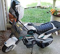 Side angle view of the white Peg Perego electric motorcycle showing body, black seat, handlebar, and front tire.