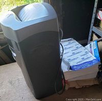Photo showing black shredder and two reams of Hammermill legal-size copy paper on a wooden surface near shelf.
