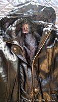 Close-up of black leather coat showing hood, zipper, and snap button closures, quilted lining visible inside.