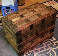Closed vintage steamer trunk showing wood slats, metal reinforcements, and worn surface with no side handles.