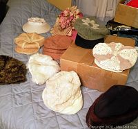 Photo showing a variety of ladies hats including faux fur, wool beret, crocheted floral and woven hats on a quilted surface