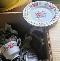 Close-up of a bone china saucer or plate with floral design of pink roses and gold rim detail.