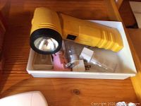Yellow flashlight with assorted plug in nightlights and LED bulbs in white tray on wooden surface
